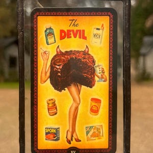 May include: A framed art piece with a vintage-style illustration. The artwork features a devil figure with a cake-like body, holding a cigarette and a drink. The background is yellow with various product images and the words "The Devil Vice".