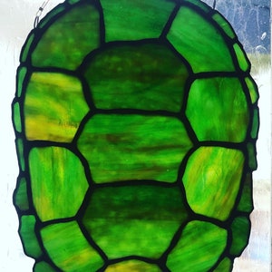 May include: A stained glass turtle shell with a green and yellow color scheme. The shell is made up of many individual pieces of glass that are joined together with black lead.
