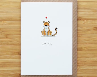 May include: A greeting card featuring a cartoon tiger with orange and black stripes, a white chest, and a red heart above its head. The words "LOVE YOU." are printed below the tiger. The card is on a brown envelope.