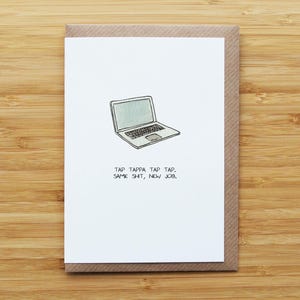 May include: A white greeting card featuring a laptop illustration and the text "TAP TAPPA TAP TAP. SAME SHIT, NEW JOB." The card has a brown border and is set on a wooden surface.