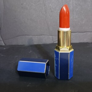 May include: A blue and gold lipstick tube with a red lipstick bullet. The tube has a hexagonal shape and the text "Christian Dior" is printed on the side.