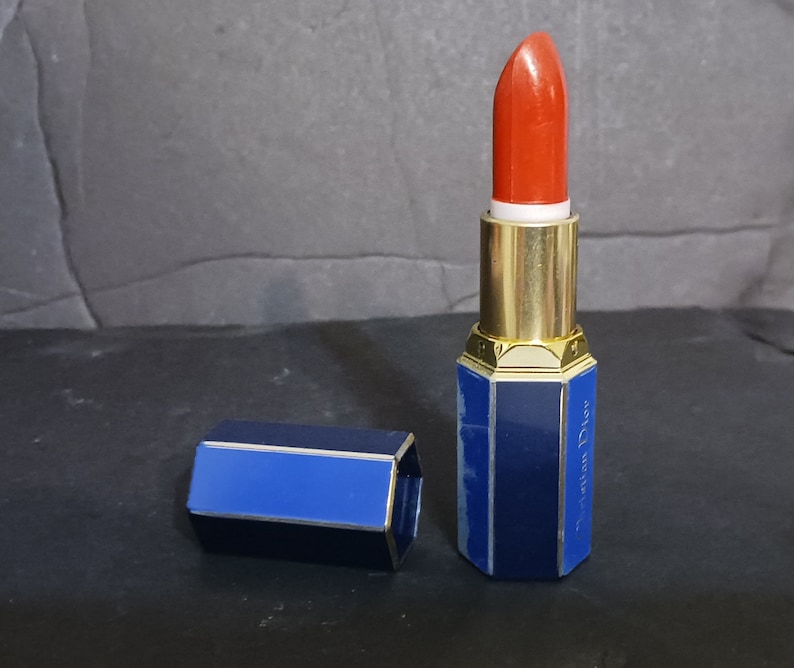 May include: A blue and gold lipstick tube with a red lipstick bullet. The tube has a hexagonal shape and the text "Christian Dior" is printed on the side.