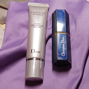 May include: Two Dior beauty products: a silver tube of Capture Totale Flash Defatiquant Regard and a blue and gold Christian Dior lipstick.