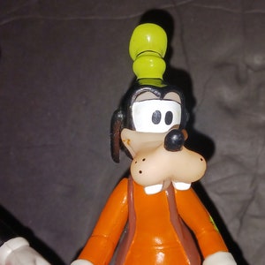 K&ouml;nnte beinhalten: Eine Comicfigur von Goofy, die einen gelben Hut und ein orangefarbenes Hemd tr&auml;gt. Er hat eine braune Nase und wei&szlig;e Augen.