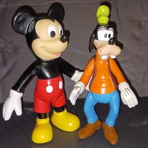 K&ouml;nnte beinhalten: Eine schwarze und rote Mickey Mouse Figur steht neben einer braunen und blauen Goofy Figur. Beide Figuren sind aus Plastik und haben einen Cartoon-Stil.