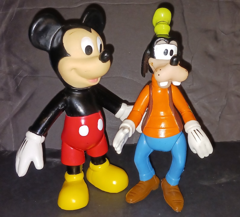 K&ouml;nnte beinhalten: Eine schwarze und rote Mickey Mouse Figur steht neben einer braunen und blauen Goofy Figur. Beide Figuren sind aus Plastik und haben einen Cartoon-Stil.