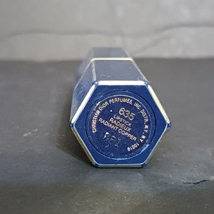 May include: A blue lipstick tube with gold lettering. The text reads "Christian Dior Perfumes, Inc. Distr., N.Y. N.Y." and "635 Lipstick Radieux Radiant Copper".