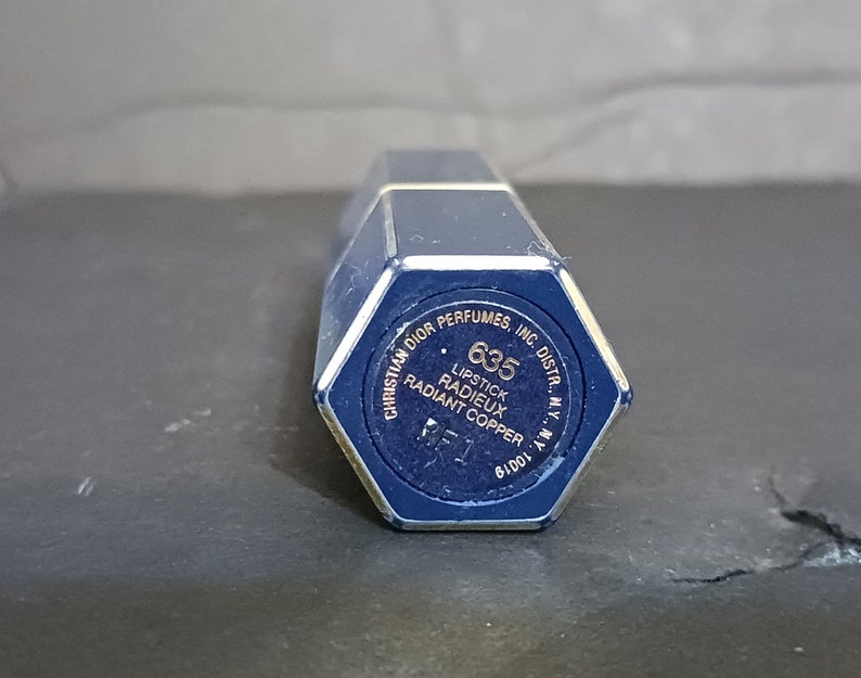 May include: A blue lipstick tube with gold lettering. The text reads "Christian Dior Perfumes, Inc. Distr., N.Y. N.Y." and "635 Lipstick Radieux Radiant Copper".
