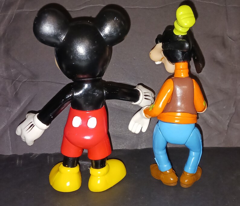 K&ouml;nnte beinhalten: Eine schwarze und rote Mickey Mouse Figur und eine braune, orange und blaue Goofy Figur. Beide Figuren stehen auf einer grauen Oberfl&auml;che.