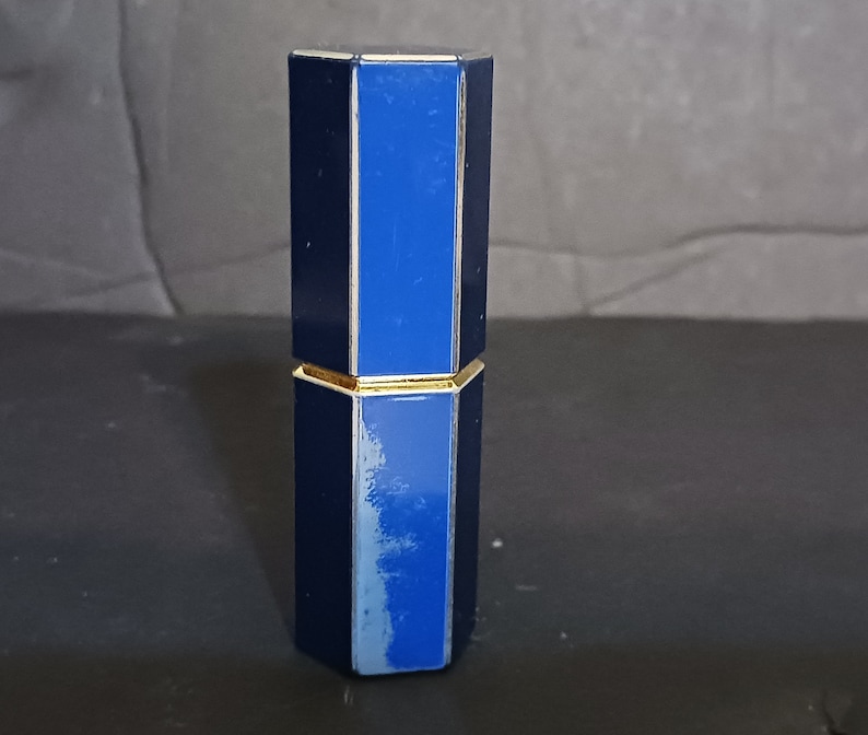 May include: A blue and gold octagonal lipstick tube with a gold band around the middle.