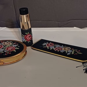 May include: A vintage vanity set with a black and gold compact mirror, a matching perfume bottle, and a black and gold embroidered makeup bag with a tassel.