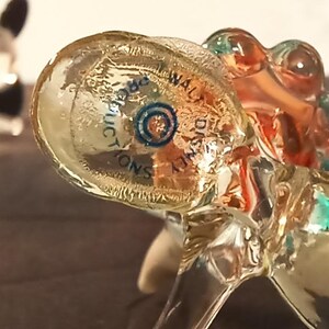 May include: Clear glass figurines with a propeller design. One figurine has black propeller blades, while the other has a multi-colored design with the text "WALT DISNEY PRODUCTIONS".