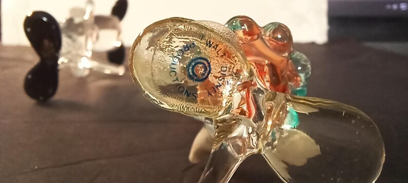 May include: Clear glass figurines with a propeller design. One figurine has black propeller blades, while the other has a multi-colored design with the text "WALT DISNEY PRODUCTIONS".