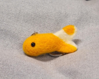 May include: A handmade felt fish keychain in yellow and white. The fish has a black eye and a key ring attached. The keychain is approximately 3 inches long.