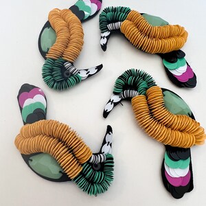 May include: Four colorful bird-shaped embellishments made of sequins and fabric. The birds are green, yellow, pink, and white.
