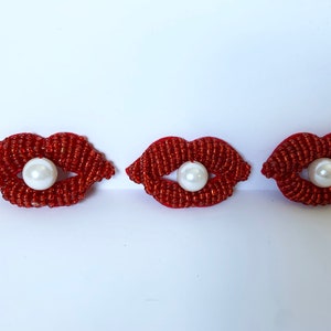 May include: Three red beaded lips with a white pearl in the centre of each.