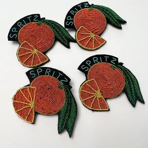 Puede incluir: Cuatro parches de planchado bordados con fondo negro, fruta cítrica naranja, hojas verdes y la palabra "SPRITZ" en fuente turquesa.