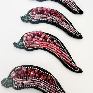 May include: Four red chili pepper shaped beaded ornaments with green stems. The peppers are made of red, clear, and silver beads.