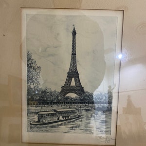 May include: A black and white drawing of the Eiffel Tower in Paris, France. The drawing shows the tower from a distance, with a boat in the foreground. The text "Paris-La Tour Eiffel" is printed below the image.
