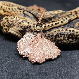 May include: A rose gold necklace featuring a delicate leaf pendant. The pendant is crafted from metal and has an intricate design.