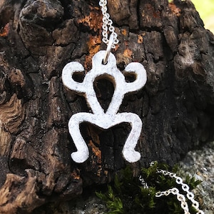 May include: A silver frog pendant necklace on a silver chain. The pendant is a stylized frog with a simple design. The necklace is resting on a piece of weathered wood.