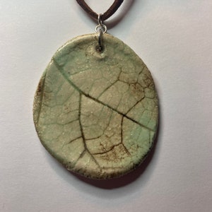 May include: A ceramic leaf pendant necklace with a brown suede cord. The leaf is a light green colour with brown veins and a crackled glaze.