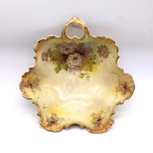 May include: A vintage, cream-coloured porcelain bowl with a floral design and gold accents. The bowl has a scalloped edge and a handle.
