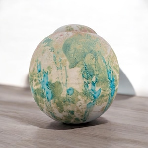 May include: A ceramic vase with a round shape and a speckled glaze in shades of green, blue, and white.