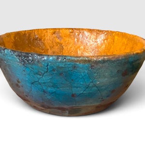 May include: A round bowl with a textured, uneven surface featuring a vibrant turquoise blue exterior with visible dark crackle patterns and a contrasting warm mustard yellow interior. The rim is irregular and the base shows dark brown tones.