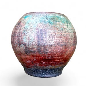 May include: A round ceramic vase with a textured surface featuring a gradient of colors. The top section is a mottled teal and white, transitioning into a deep red middle band, and finishing with a dark charcoal gray base with a rough finish.
