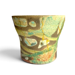 May include: A ceramic vessel featuring a flared rim and a tapered base, decorated with a marbled pattern of green, brown, and cream tones. The surface displays visible cracks repaired with gold-colored lacquer, highlighting the kintsugi technique.