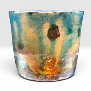 May include: A cylindrical ceramic planter featuring a crackled glaze finish with a blend of turquoise, teal, and golden yellow hues. The surface displays dark brown spots and a textured, bubbly appearance near the base, creating a multi-coloured effect.