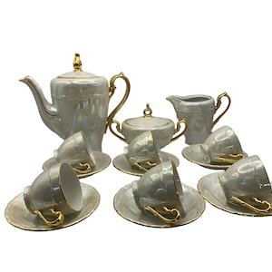 May include: A white porcelain tea set with gold accents. The set includes a teapot, creamer, sugar bowl, and six cups and saucers. The cups and saucers have a pearlescent finish.