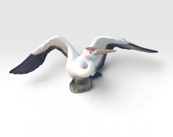 Könnte beinhalten: Eine Porzellanfigur eines Vogels im Flug mit weit ausgebreiteten Flügeln. Der Vogel hat einen weißen Körper, dunkel blaugraue Flügelspitzen und einen kleinen braunen Fleck auf dem Kopf. Er besitzt einen langen, spitzen Schnabel und einen grauen Sockel.