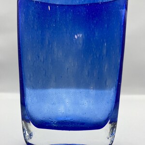 K&ouml;nnte beinhalten: Eine blaue Glasvase mit strukturierter Oberfl&auml;che. Die Vase hat eine abgerundete rechteckige Form und einen klaren Glasboden.