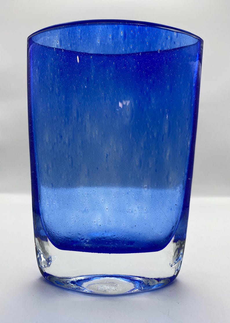 K&ouml;nnte beinhalten: Eine blaue Glasvase mit strukturierter Oberfl&auml;che. Die Vase hat eine abgerundete rechteckige Form und einen klaren Glasboden.