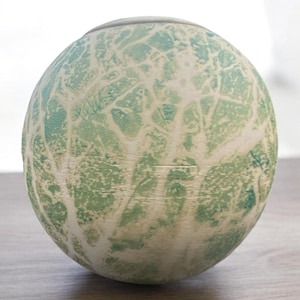 May include: A round ceramic vase with a white and green abstract design. The vase has a smooth, glossy finish.
