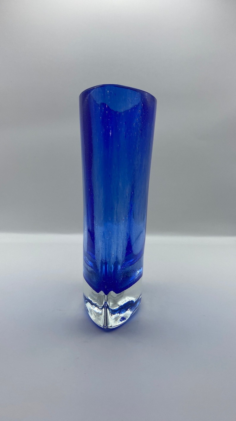 K&ouml;nnte beinhalten: Eine kobaltblaue Glasvase mit einem klaren Glasfu&szlig;. Die Vase hat eine abgerundete, leicht ausgestellte &Ouml;ffnung und einen spitzen Fu&szlig;.