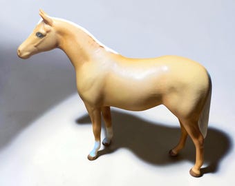 Könnte beinhalten: Eine stehende Pferdefigur mit hellbraunem Fell, weißer Mähne und weißem Schweif. Das Pferd hat weiße Abzeichen an den unteren Beinen und dunkelbraune Hufe. Die Figur ist in einer glatten, matten Oberfläche mit realistischer Haltung gefertigt.