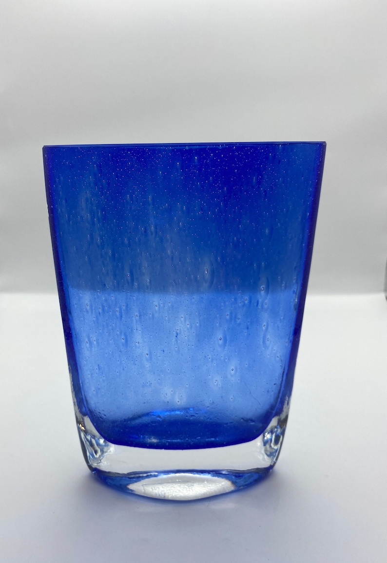 K&ouml;nnte beinhalten: Eine blaue Glasvase mit strukturierter Oberfl&auml;che. Die Vase hat einen klaren Boden und eine abgerundete rechteckige Form.
