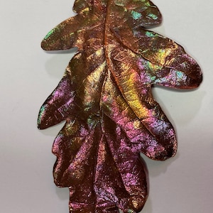 May include: A copper leaf pendant with an iridescent finish. The leaf is detailed with veins and has a loop at the top for hanging.