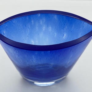 K&ouml;nnte beinhalten: Eine kleine, blaue Glassch&uuml;ssel mit leicht ovaler Form. Die Sch&uuml;ssel hat ein wei&szlig;es, wolkiges Aussehen mit einem dunkelblauen Rand.