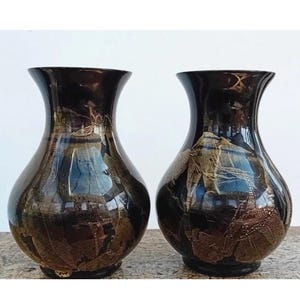 May include: Two black ceramic vases with gold and brown abstract designs. The vases are round with a wide base and a narrow neck.