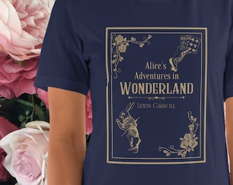 May include: Navy blue t-shirt featuring a gold-colored framed graphic from "Alice's Adventures in Wonderland." The graphic includes the title, a rabbit, and playing cards. The author's name, Lewis Carroll, is also included.