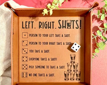 May include: A brown leather shot tray with the text "LEFT. RIGHT. SHOTS!" and instructions for a drinking game. A white die with black dots is on the tray. The tray has a rectangular shape with raised edges.
