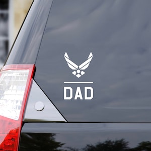 May include: A white vinyl decal with the United States Air Force logo and the word "DAD" on a black car window.
