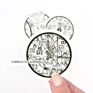 May include: A black and white circular sticker with a detailed map of the Charleston AFB/INTL airport. The sticker includes the airport's identifier (CHS), altitude (40 SFC), and other navigational information.