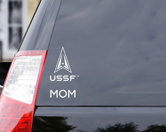 May include: A white vinyl sticker with a stylised arrow design and the text "USSF" and "MOM" on a black car.