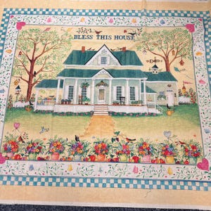 May include: A rectangular fabric panel featuring a printed illustration of a house with a green roof and white siding. The text BLESS THIS HOUSE is centred above the house. The scene includes trees, flowers, birds, and a blue checkered border.
