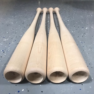 May include: Four unfinished wooden baseball bats, arranged in a row, with the rounded ends facing the camera.